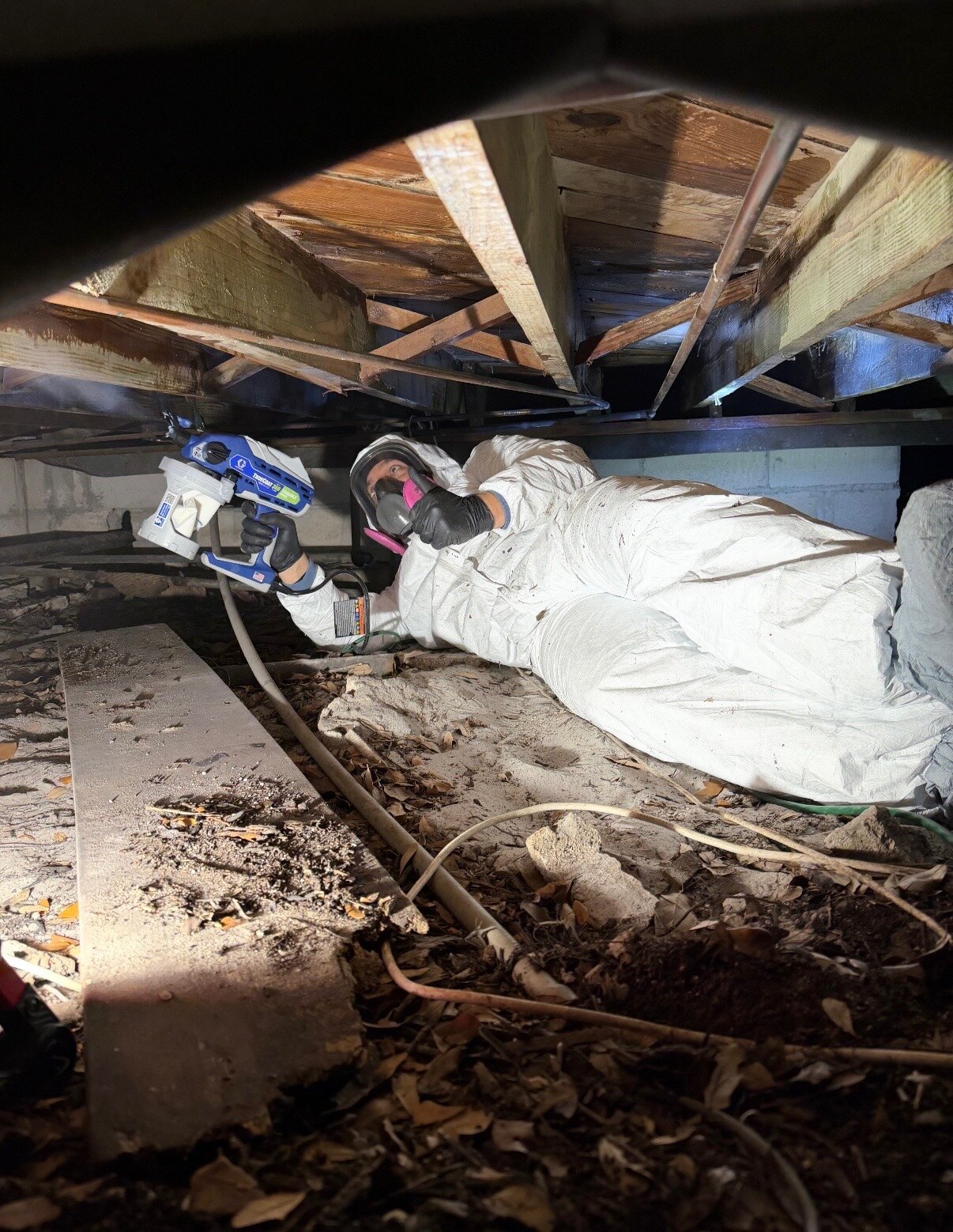 Technician treating a crawlspace in full protective gear